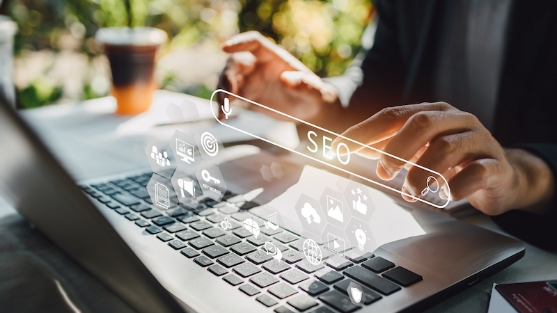Hands typing on a laptop keyboard with holographic SEO icons and a search bar overlay, symbolizing digital marketing, search engine optimization, and efforts to remove negative content from Google. A blurred coffee cup is in the background.